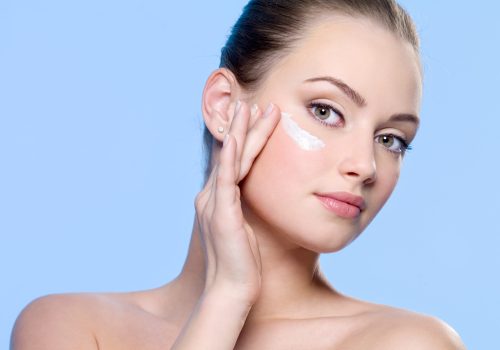 Young woman applying cream on her face - blue background